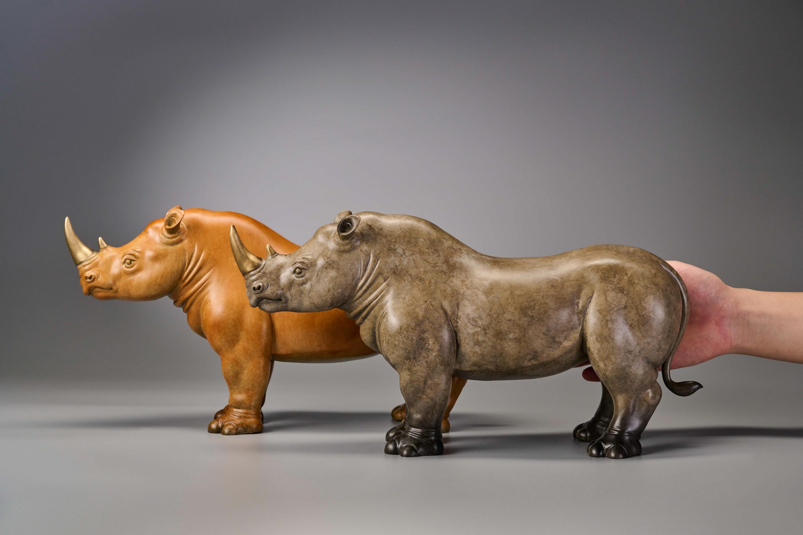 Pair of stylized rhinos in amber and grey — pair with hand scale.