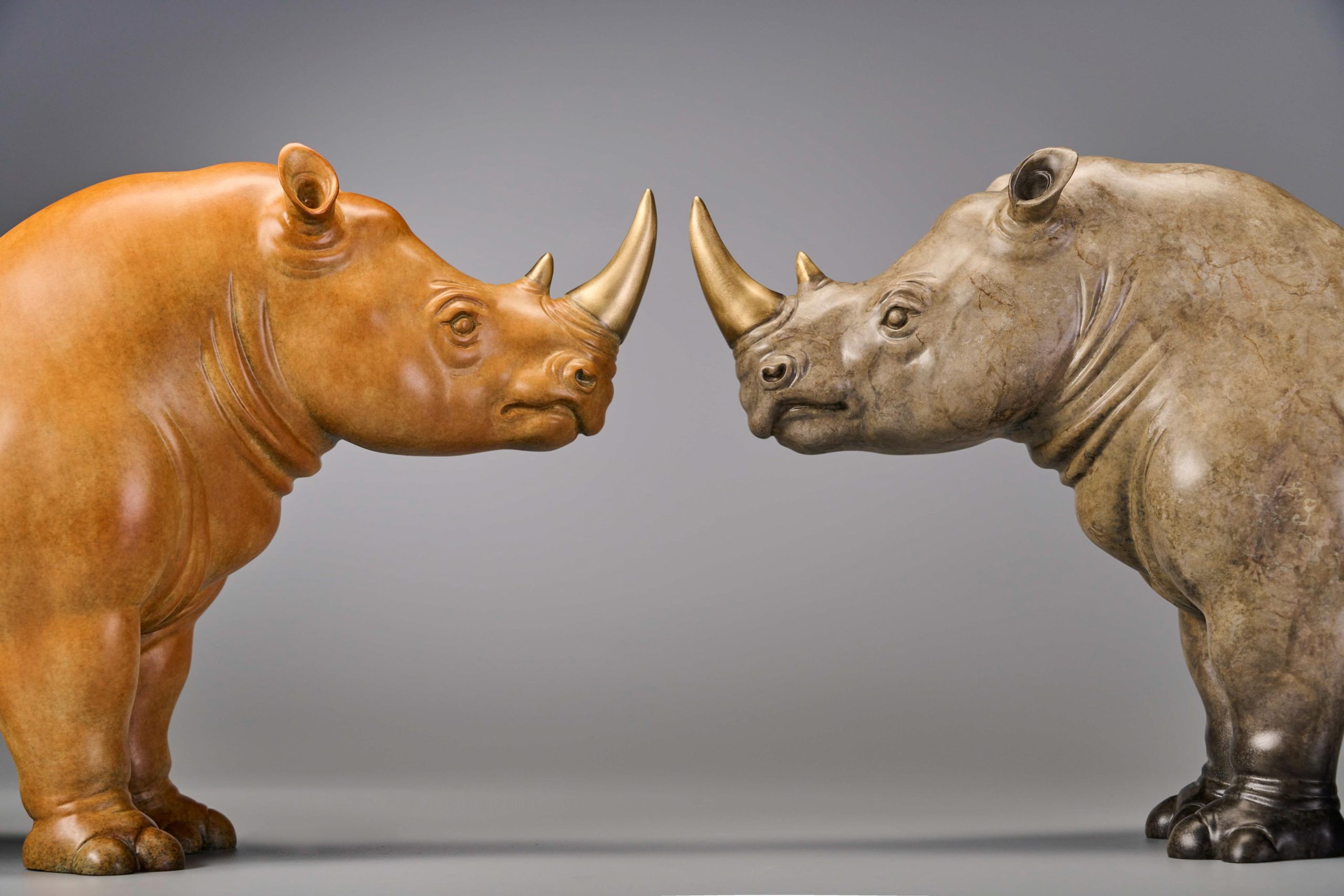 Pair of stylized rhinos in amber and grey — pair facing each other.