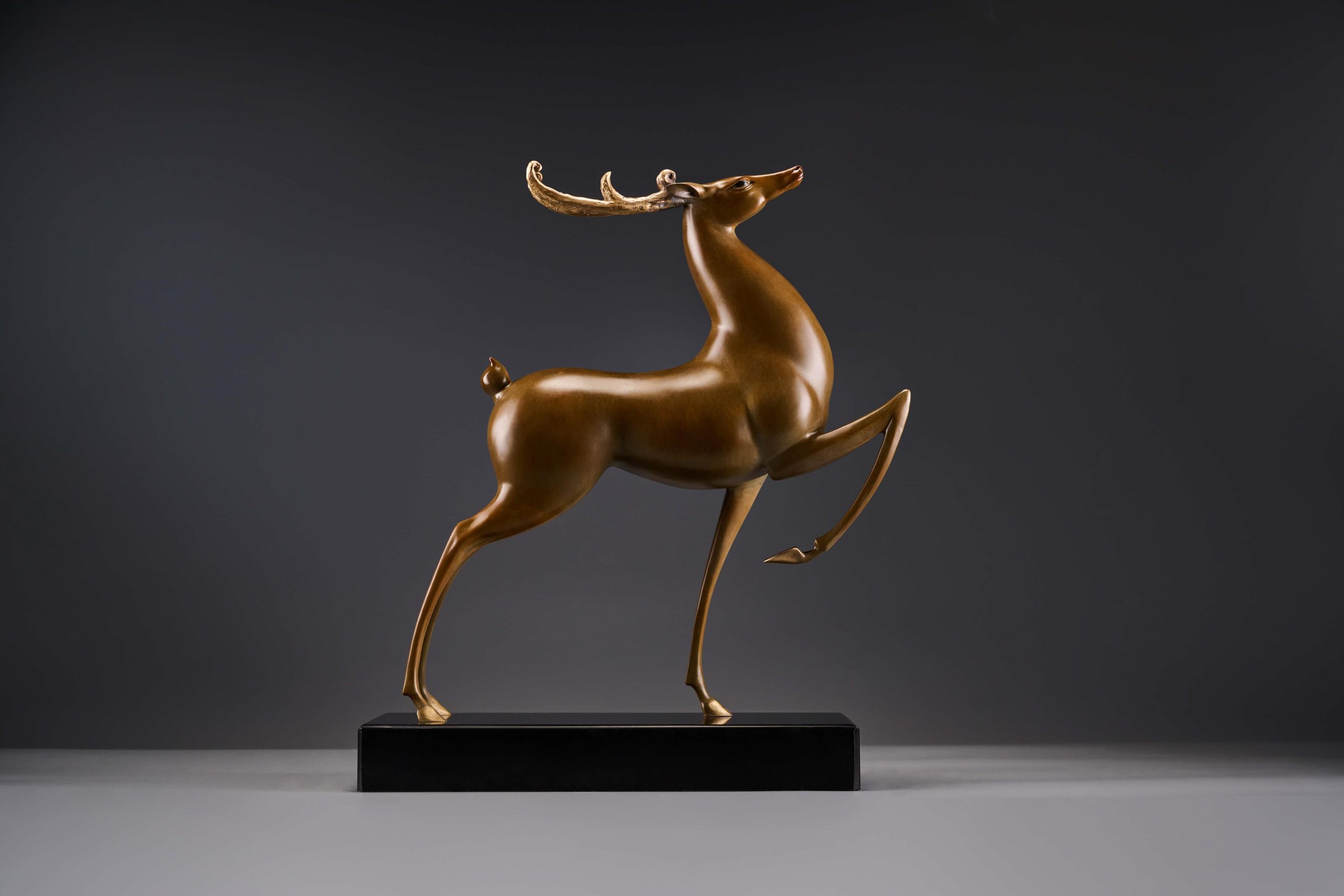 Prancing bronze deer with golden antlers — opposite three-quarter.
