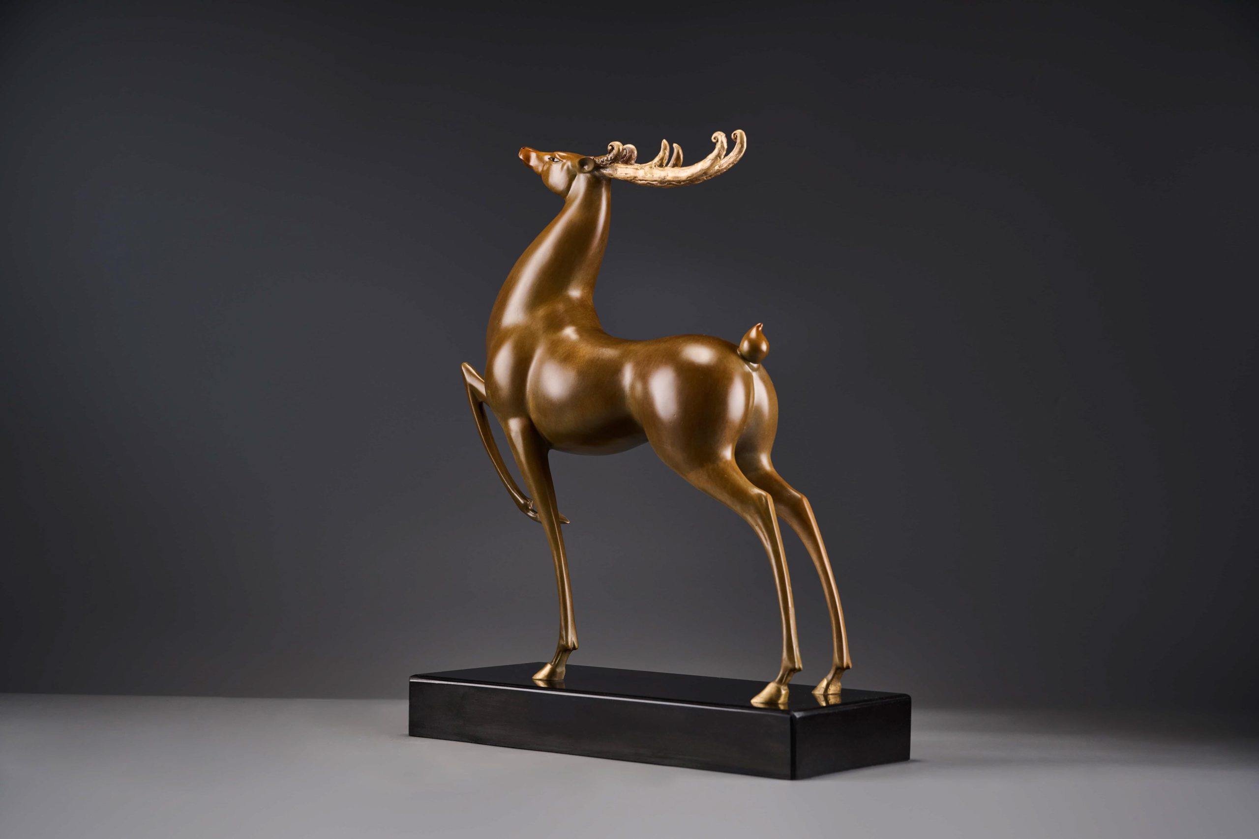 Prancing bronze deer with golden antlers — front view.