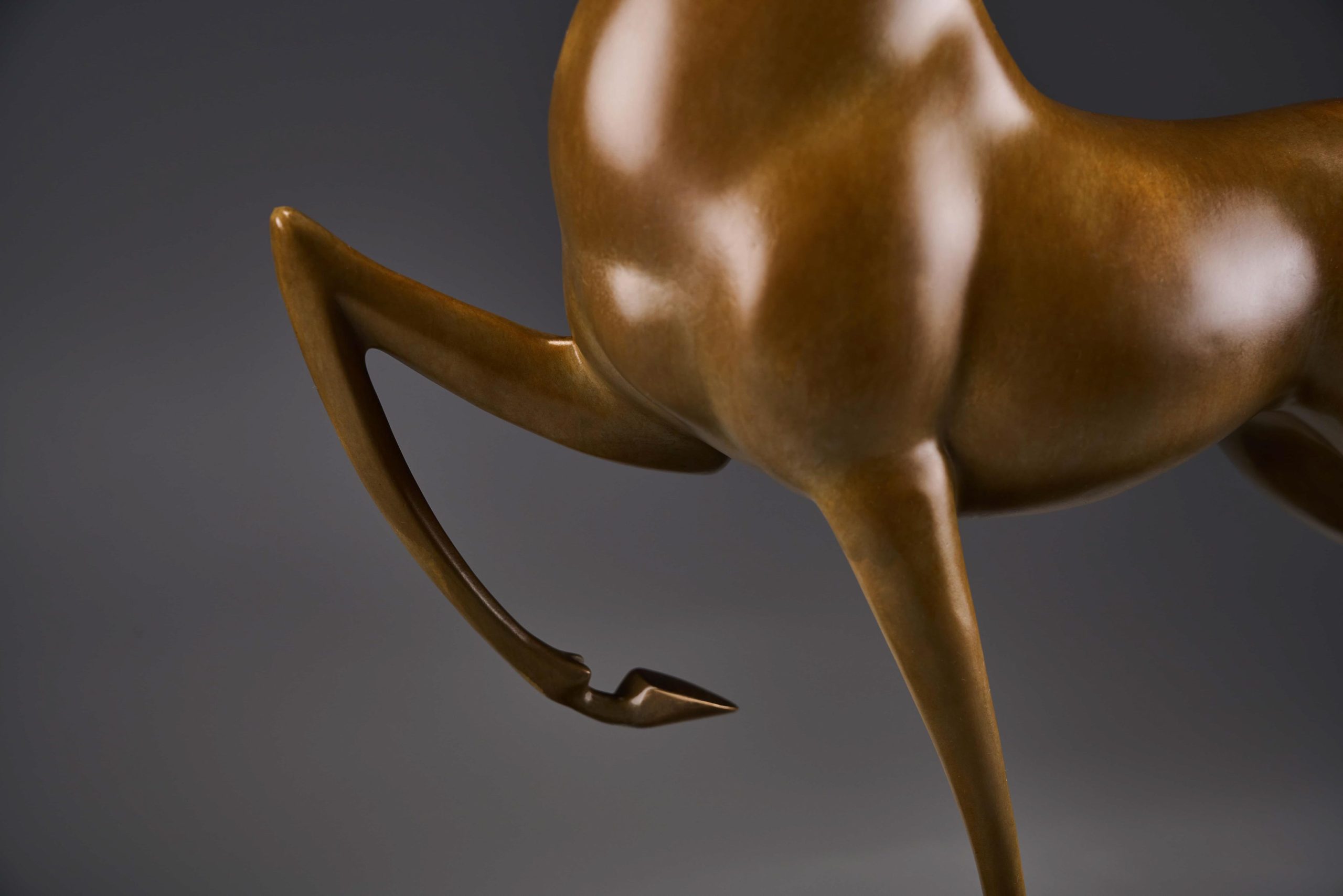 Prancing bronze deer with golden antlers — foreleg detail.
