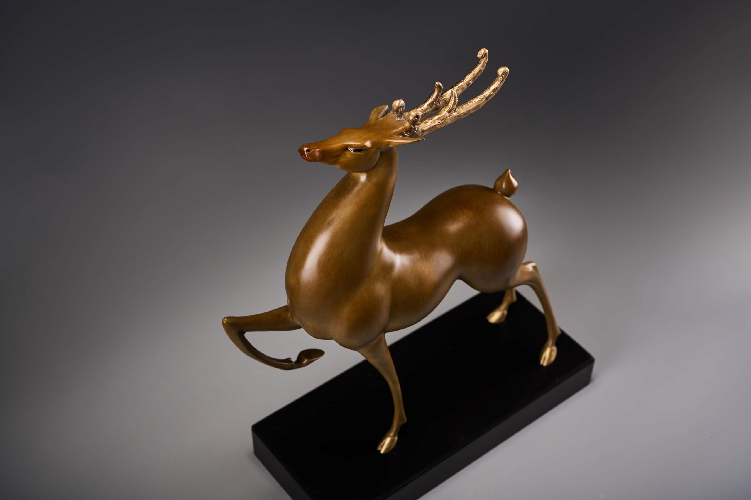 Prancing bronze deer with golden antlers — front three-quarter.