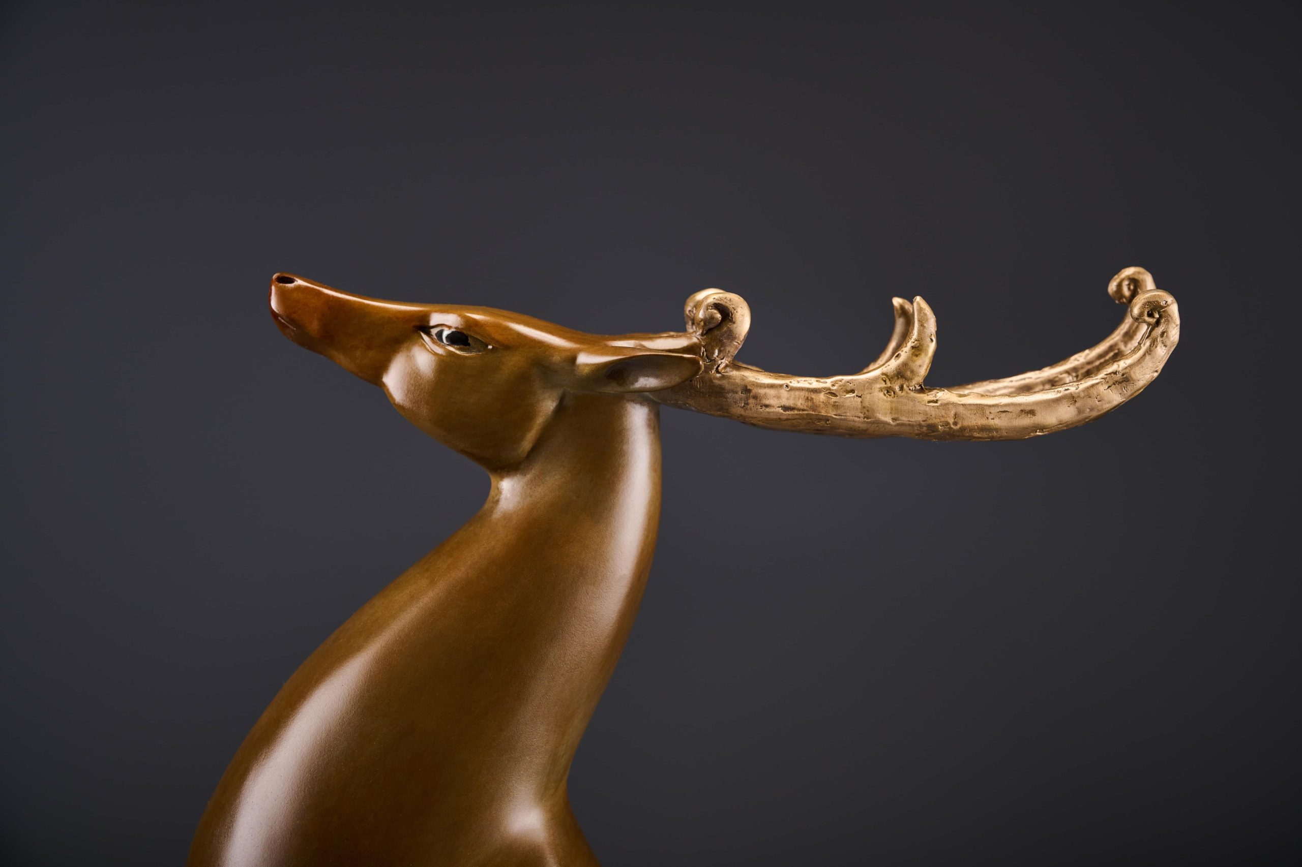 Prancing bronze deer with golden antlers — head and antler close-up.