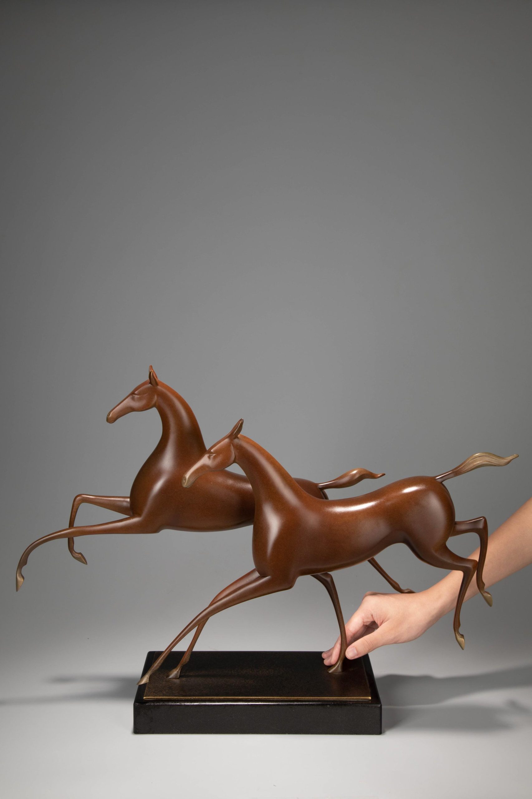 Running horse pair in warm sienna — three-quarter with hand scale.