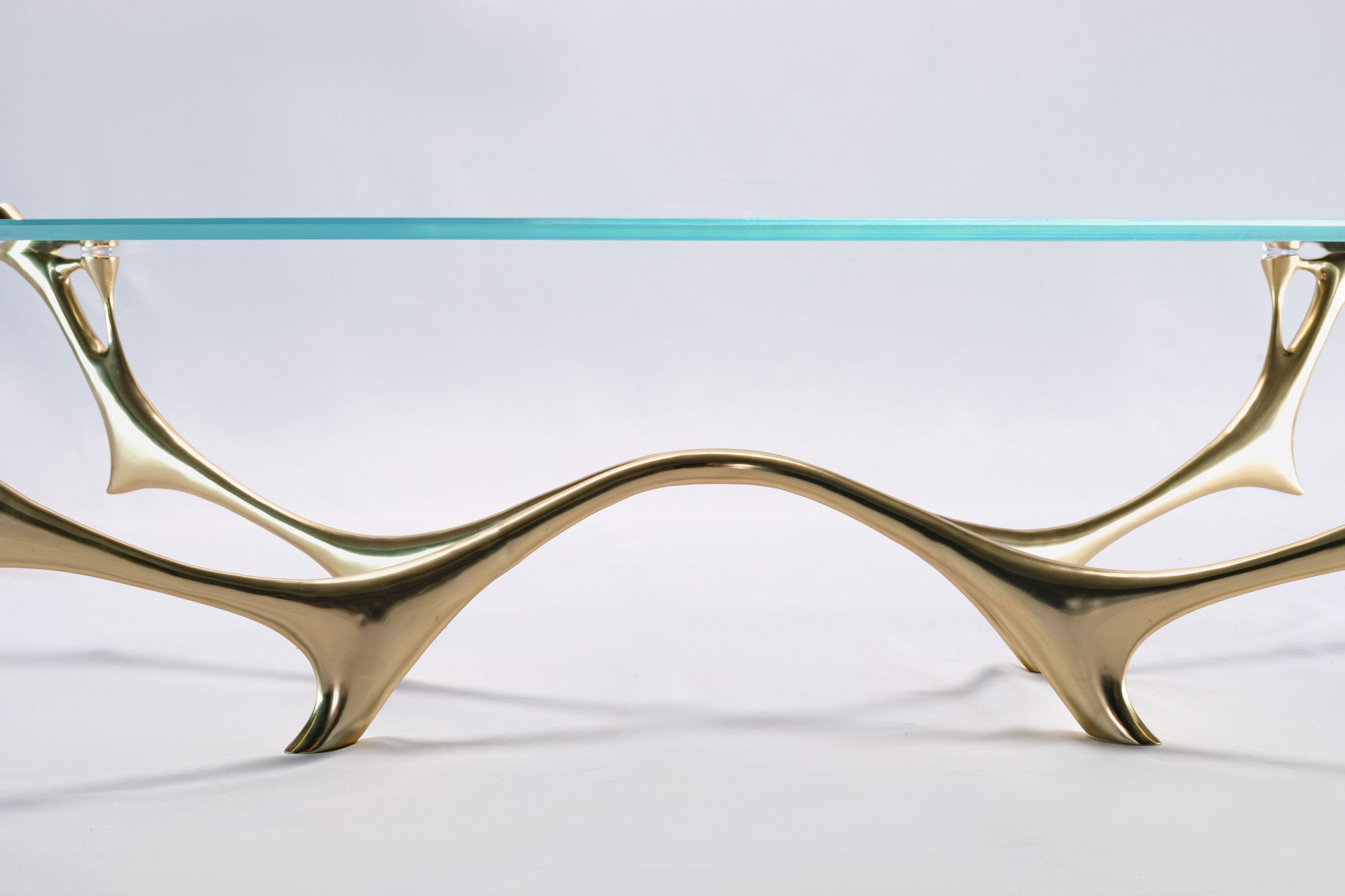 Bronze coffee table with oval glass top, front view showing water-and-branch silhouette base