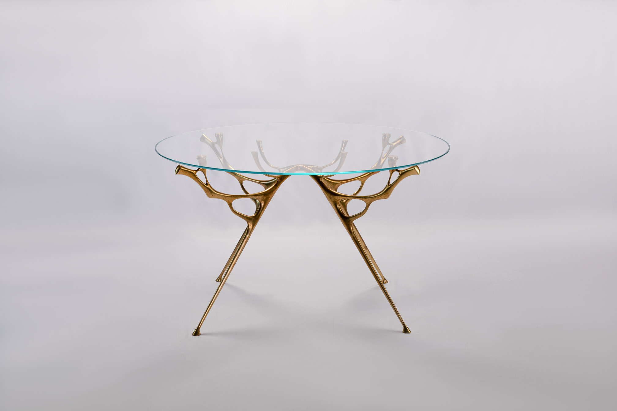Round bronze dining table with water-and-branch base, angled view