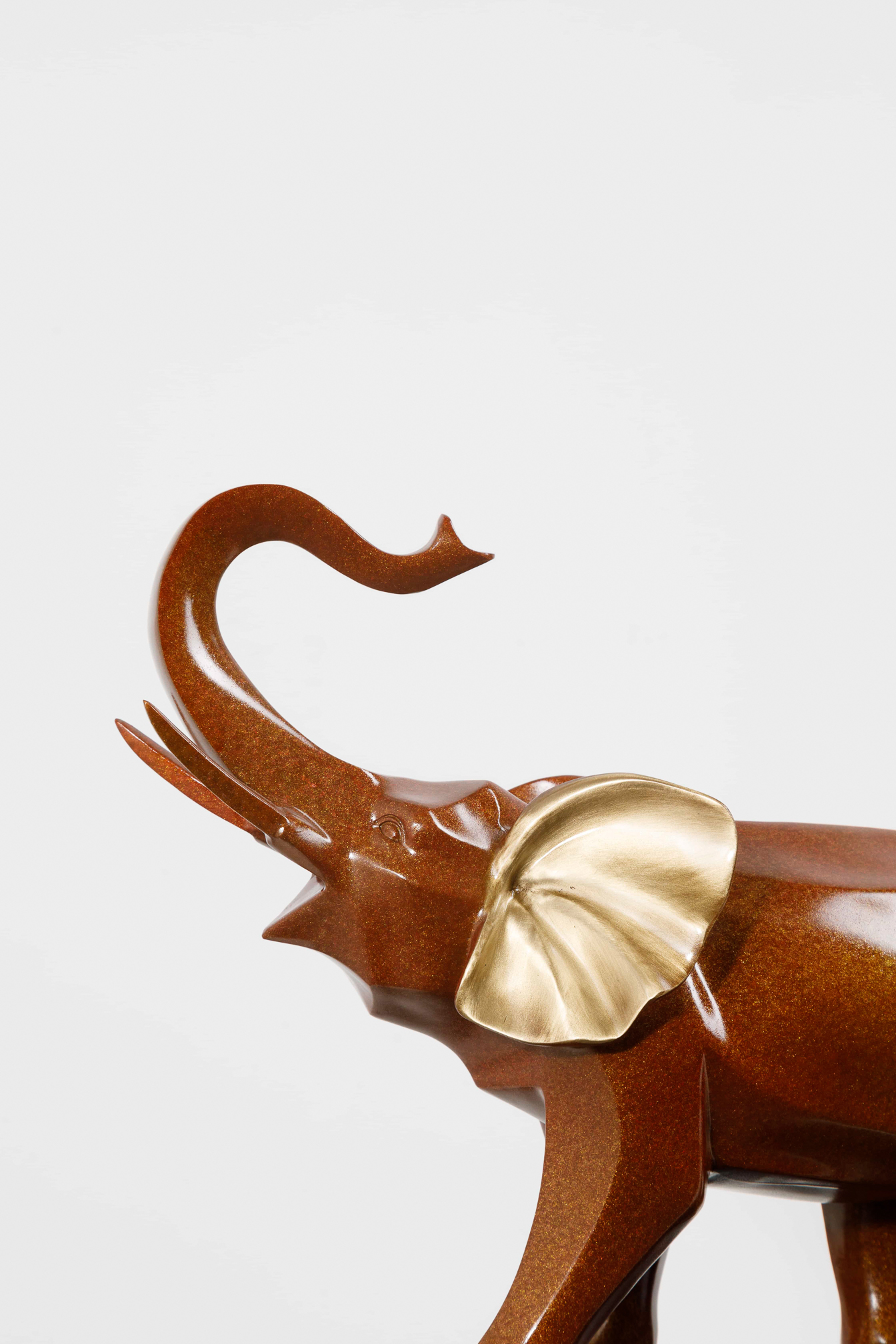 Mahogany-brown elephant family with gold ears — raised trunk close-up.