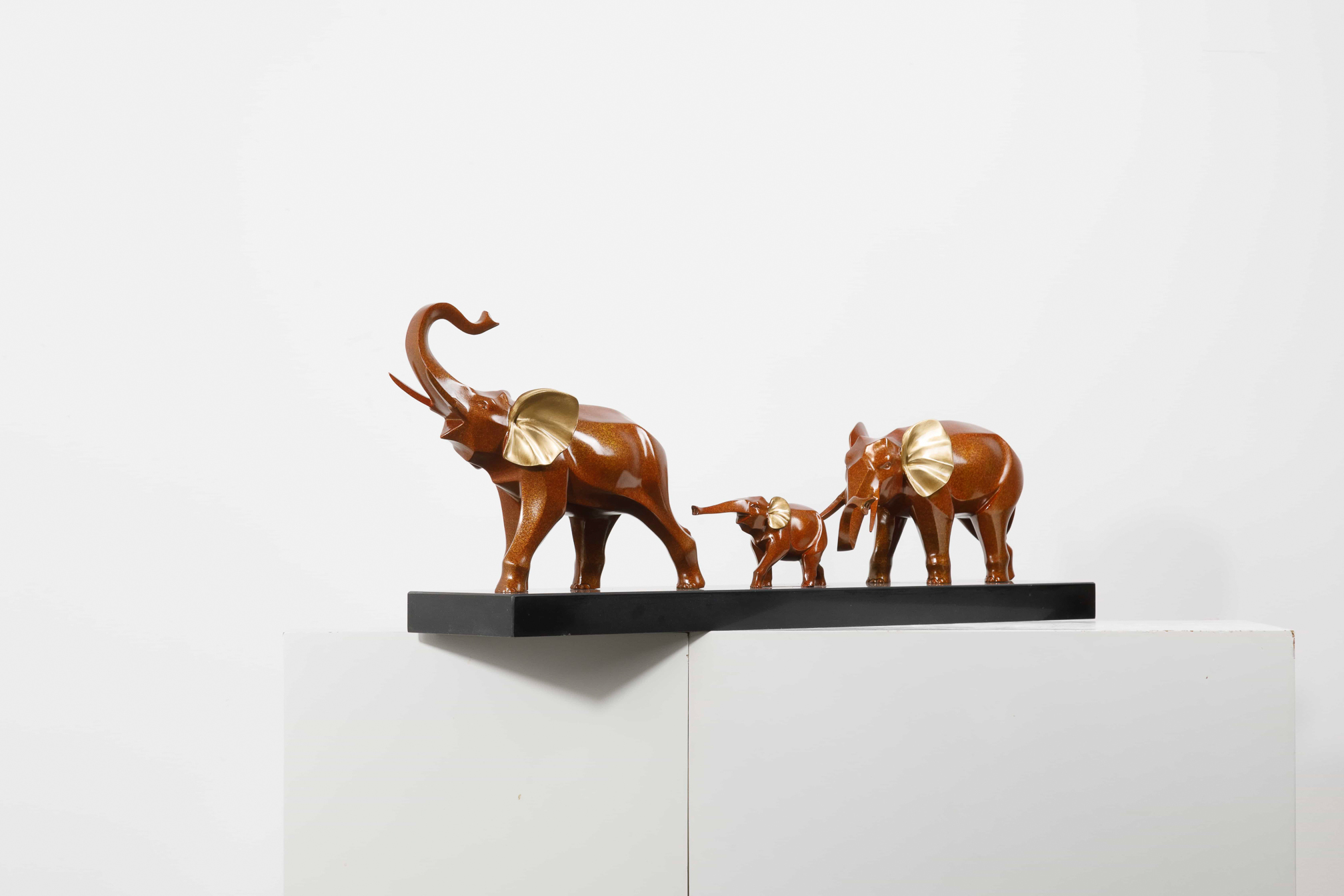 Mahogany-brown elephant family with gold ears — group alt angle.