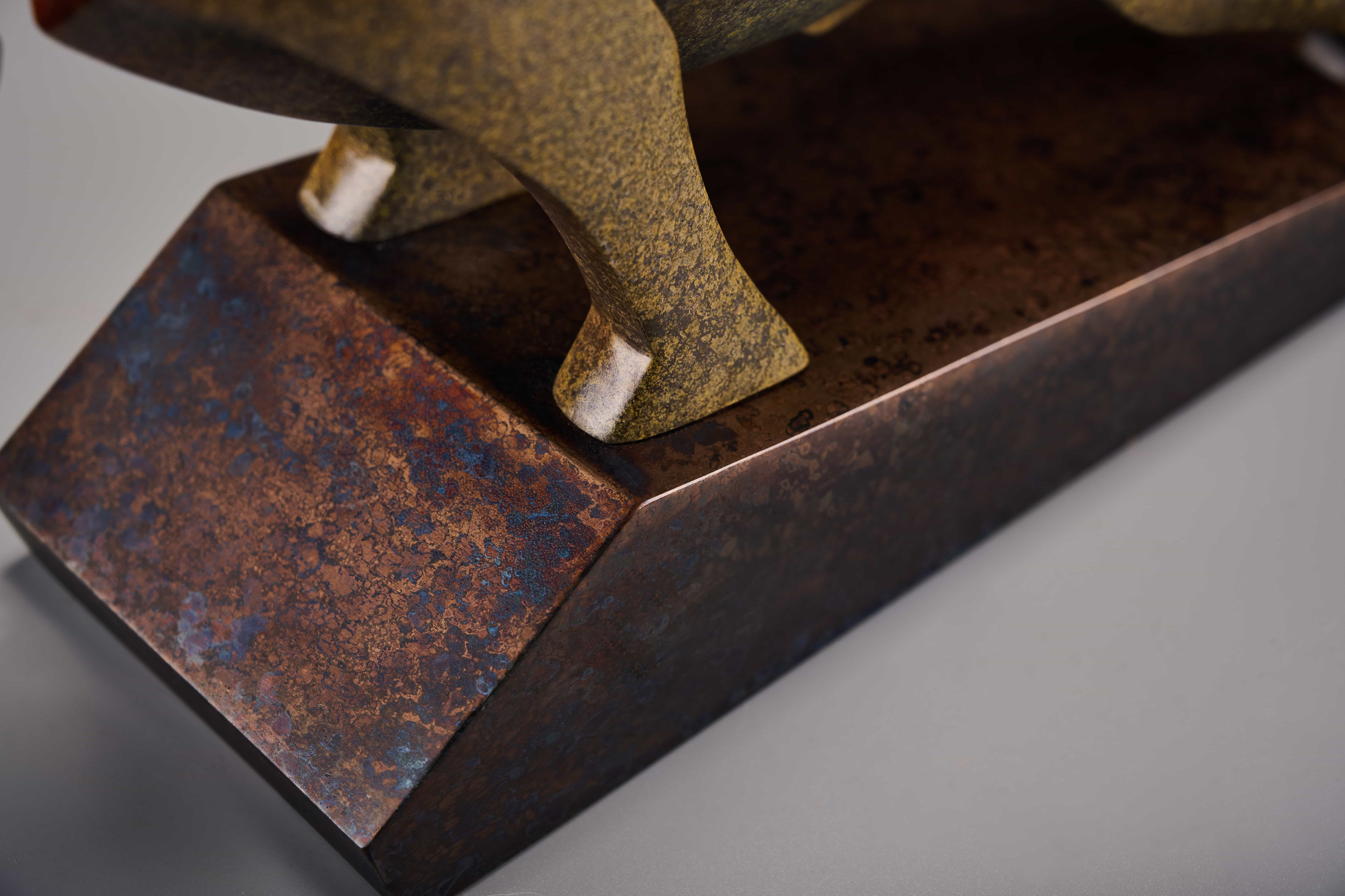 Abstract charging bull with red crest — base corner detail.