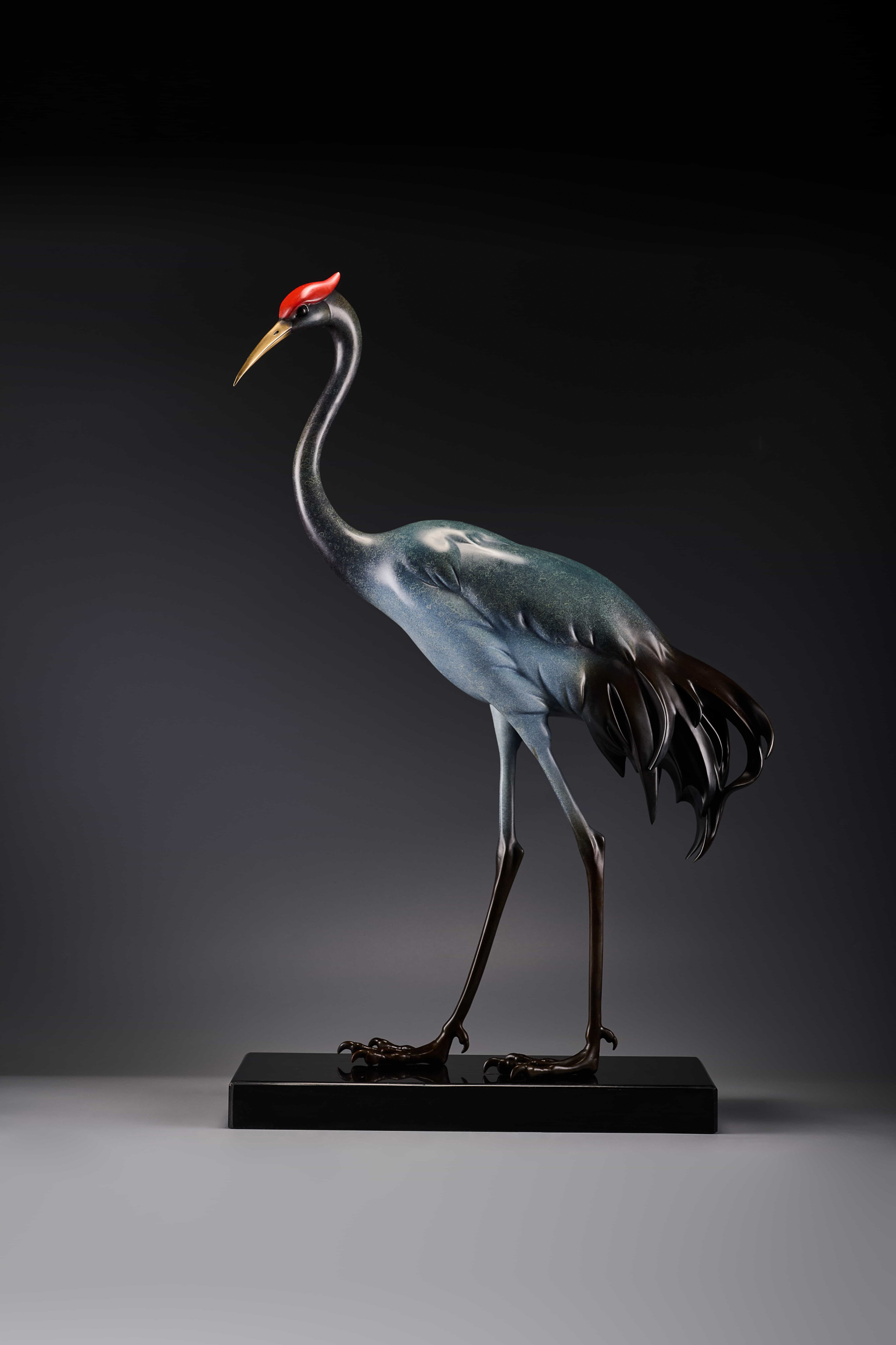 Silver-blue crane with red crown on black base — front view.