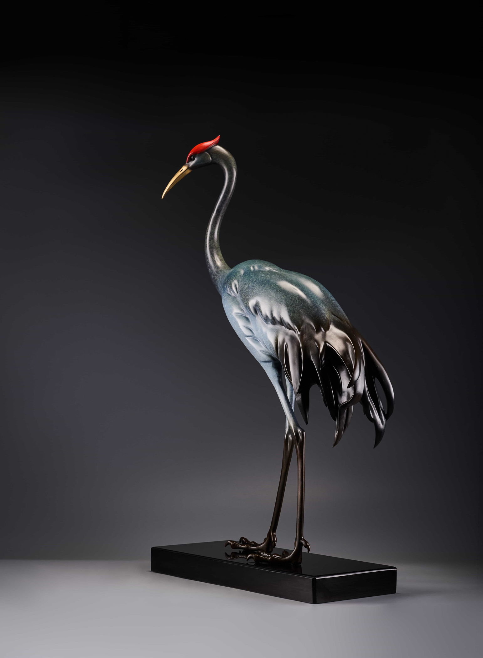 Silver-blue crane with red crown on black base — side view.