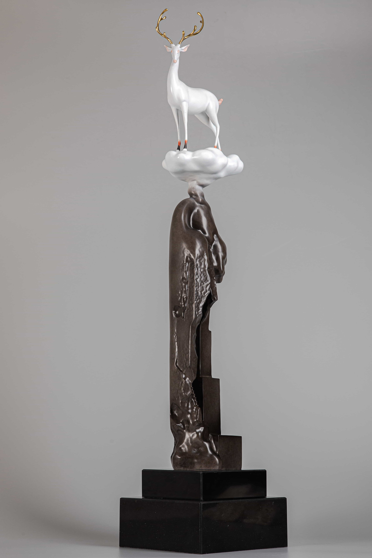 White deer on tall bronze cliff column — alt angle view.
