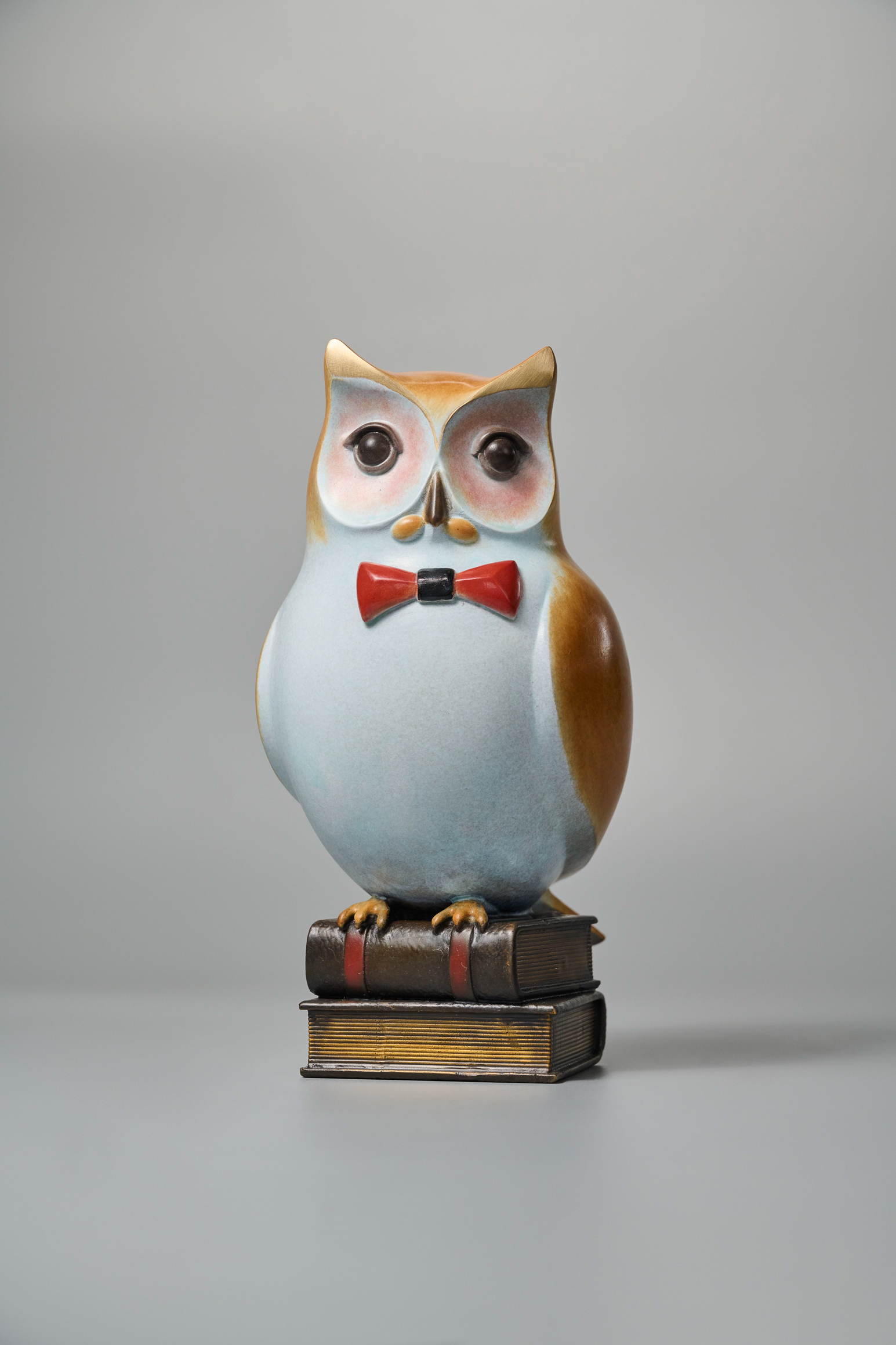 Cartoon owl with red bow tie on books — front alt angle.