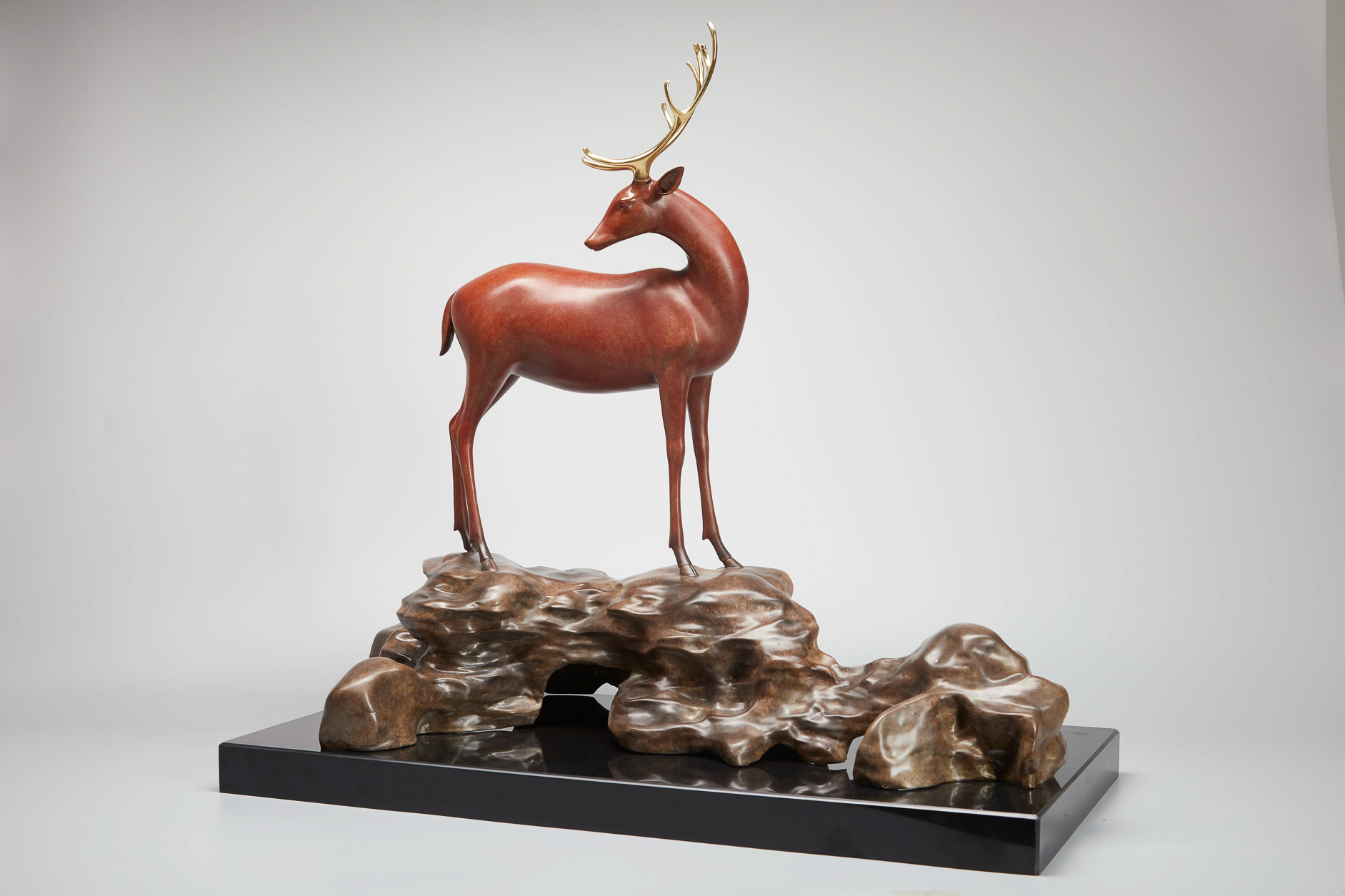 Red-brown deer with golden antlers on rock base — alt angle view.