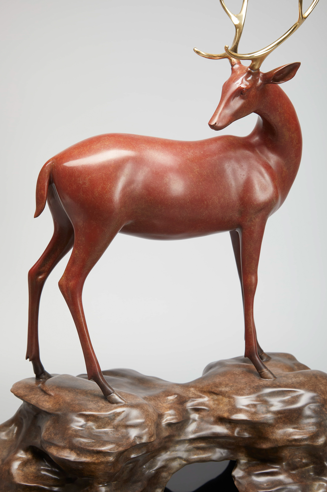 Red-brown deer with golden antlers on rock base — front view.