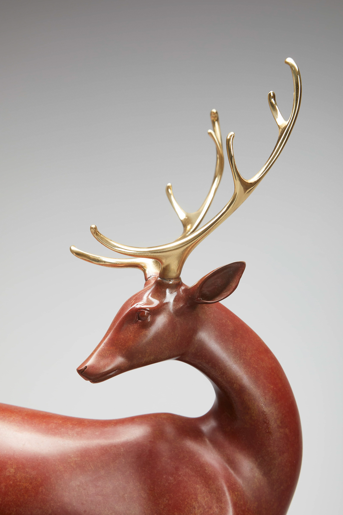 Red-brown deer with golden antlers on rock base — head and antlers close-up.