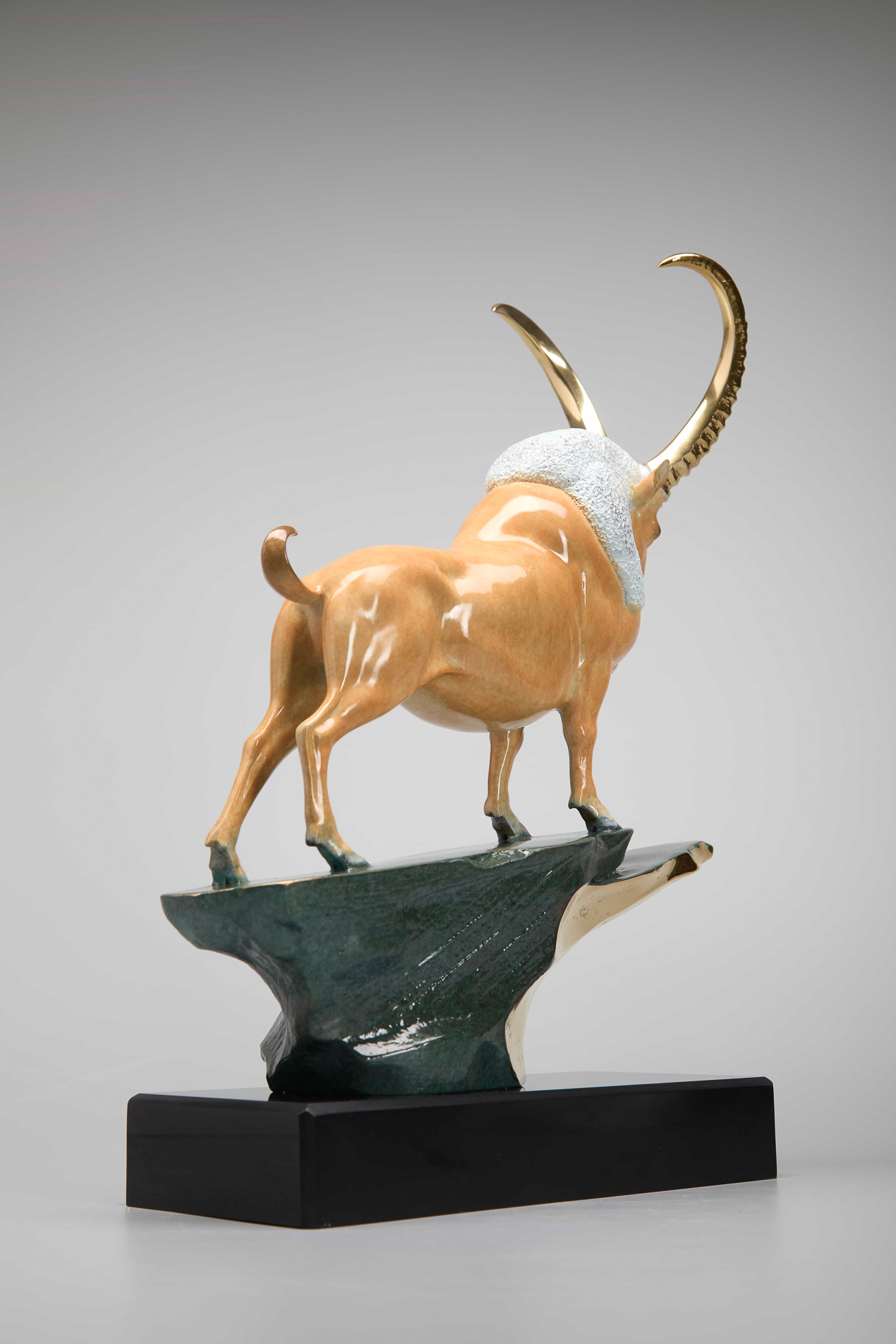 Golden ibex on green-and-gold cliff base — rear view.