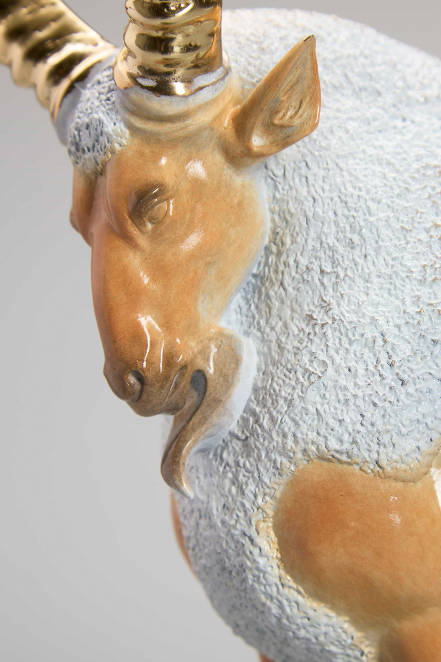 Golden ibex on green-and-gold cliff base — head and horn close-up.