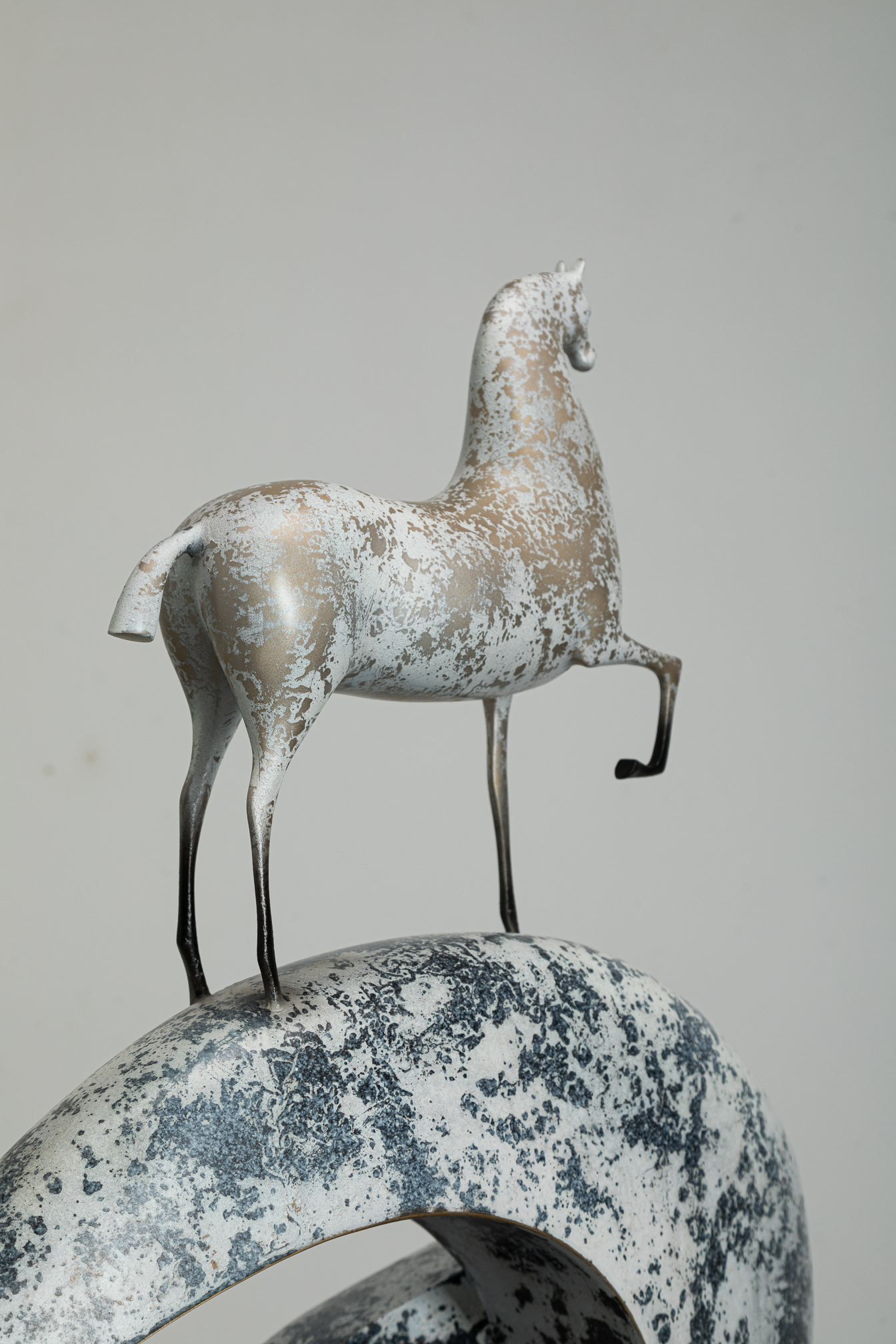White horse climbing blue-and-white mottled arc base — close three-quarter.