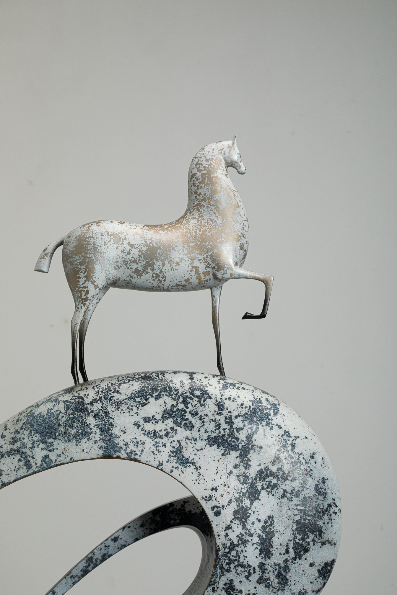 White horse climbing blue-and-white mottled arc base — near three-quarter.