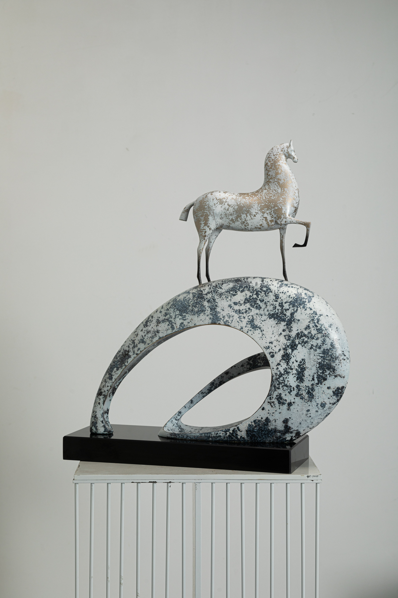 White horse climbing blue-and-white mottled arc base — front view.