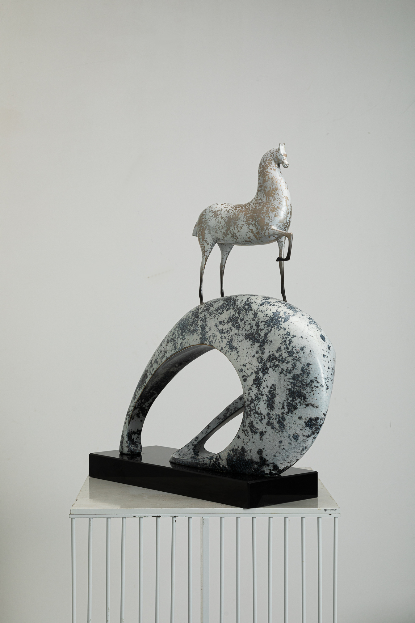 White horse climbing blue-and-white mottled arc base — side view.