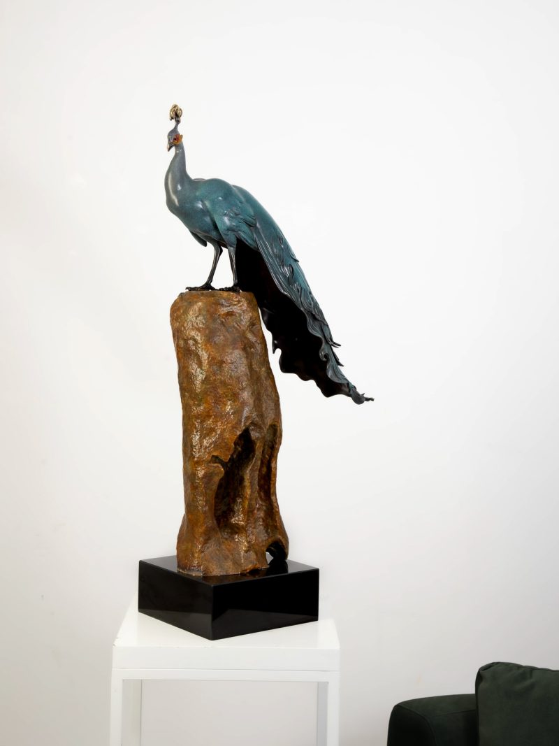 Patina-green peacock standing on tall rock — main side view.