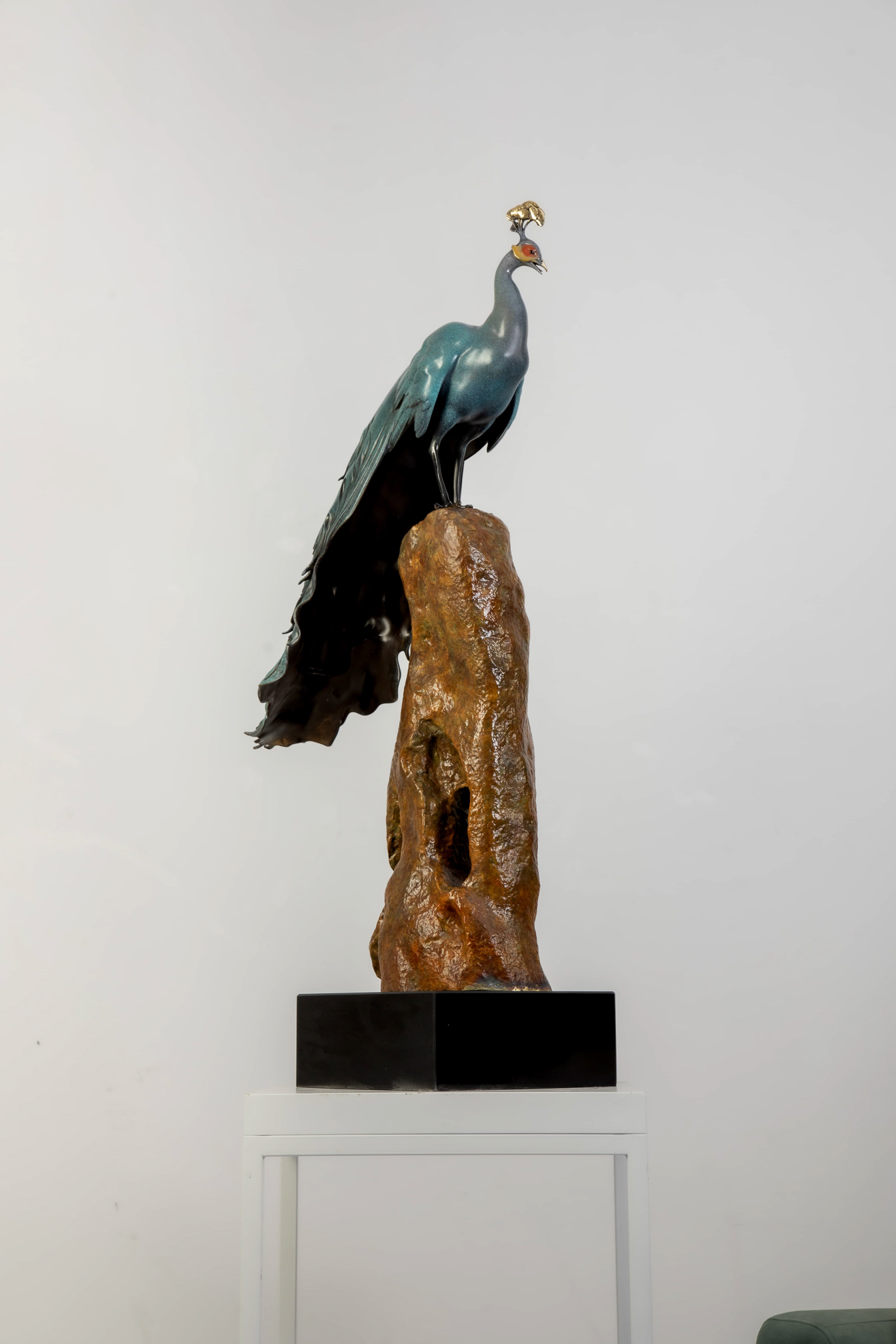 Patina-green peacock standing on tall rock — front view.
