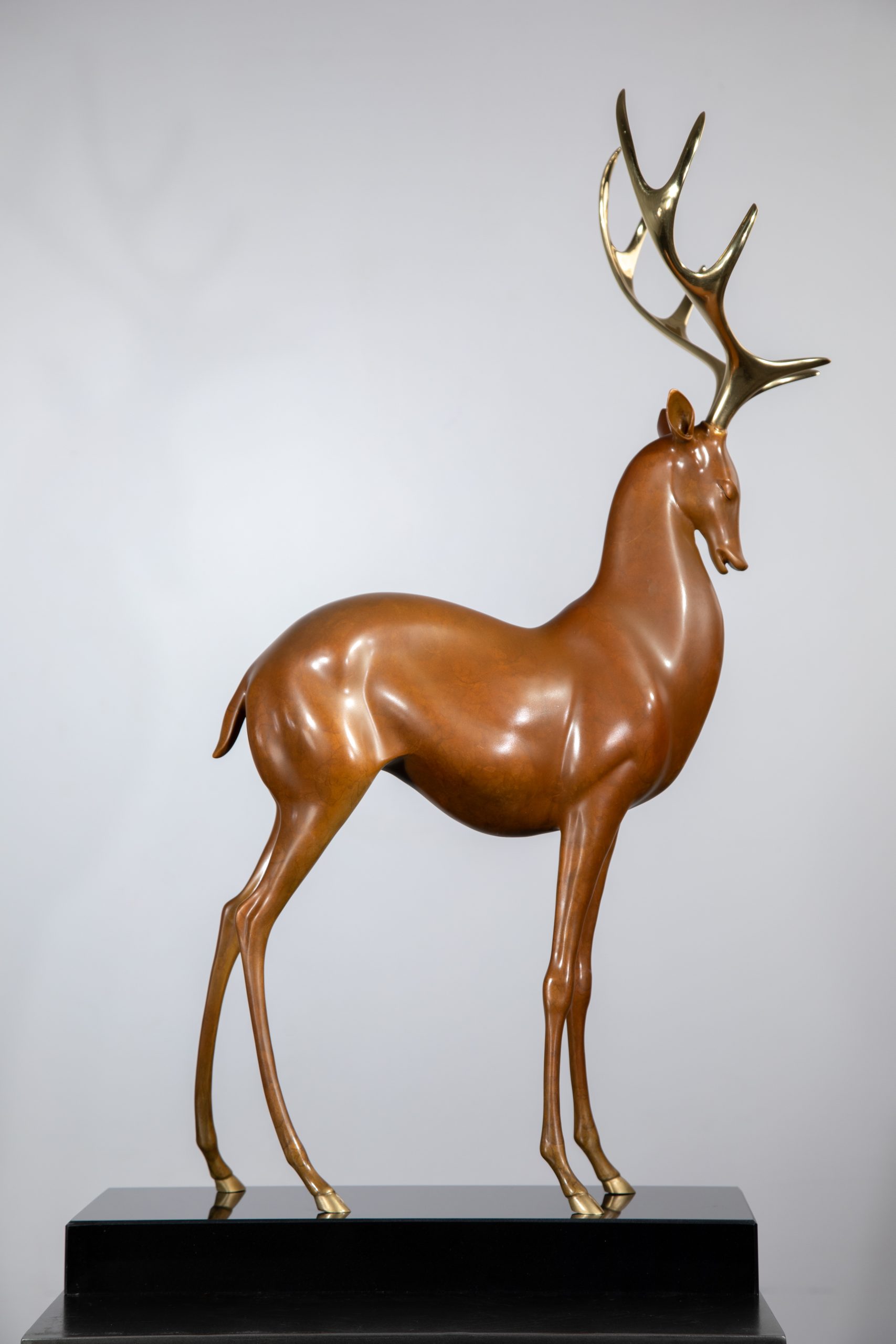 Brown deer with golden antlers on black base — front.