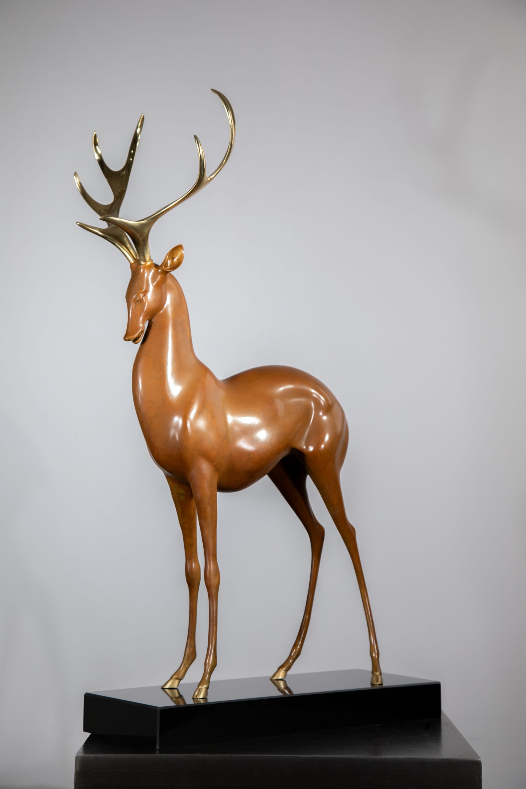 Brown deer with golden antlers on black base — side.